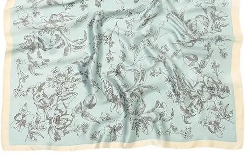 Pale blue silk scarf laid flat with a fine botanical line design