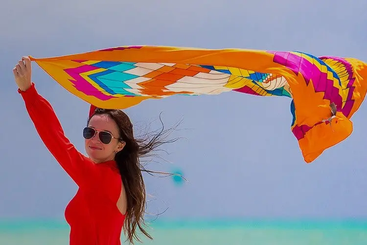 Woman holding a brightly printed silk scarf open in the wind