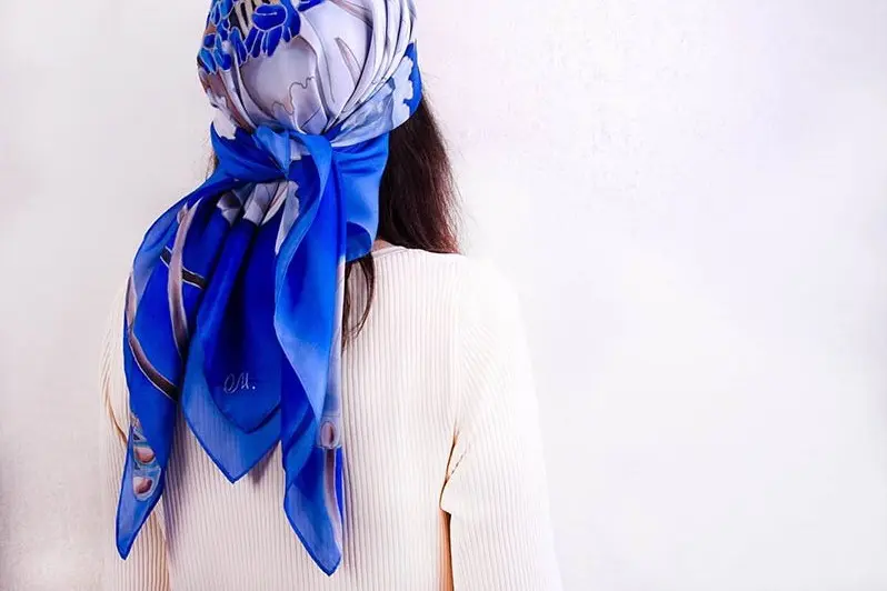 Large blue printed silk scarf tied over a ribbed knit top