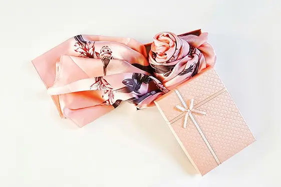 Pink printed silk scarf arranged beside a ribboned gift box