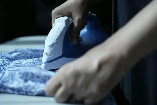 Hands moving an iron across patterned fabric on an ironing board