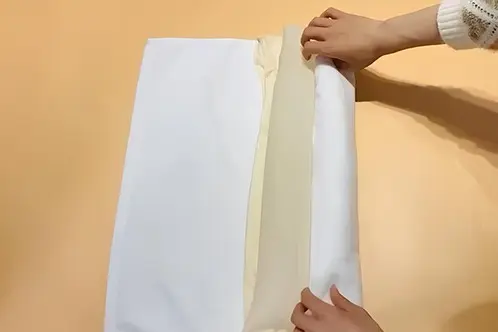 Hands folding a clean towel around a silk pillowcase to press out excess water